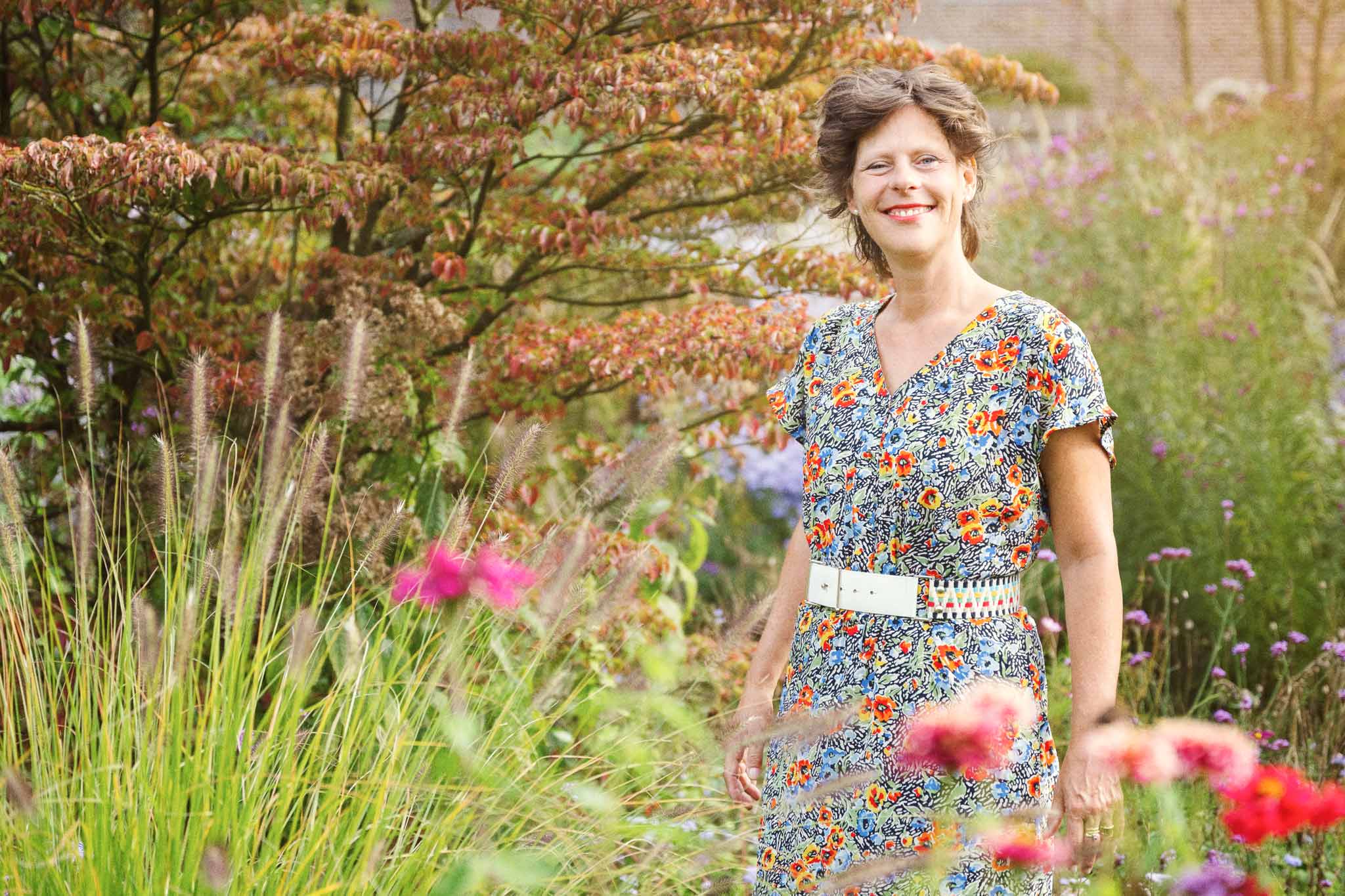 Exterior photo of a smiling Carina Weijma standing among flowers in a luscious park.